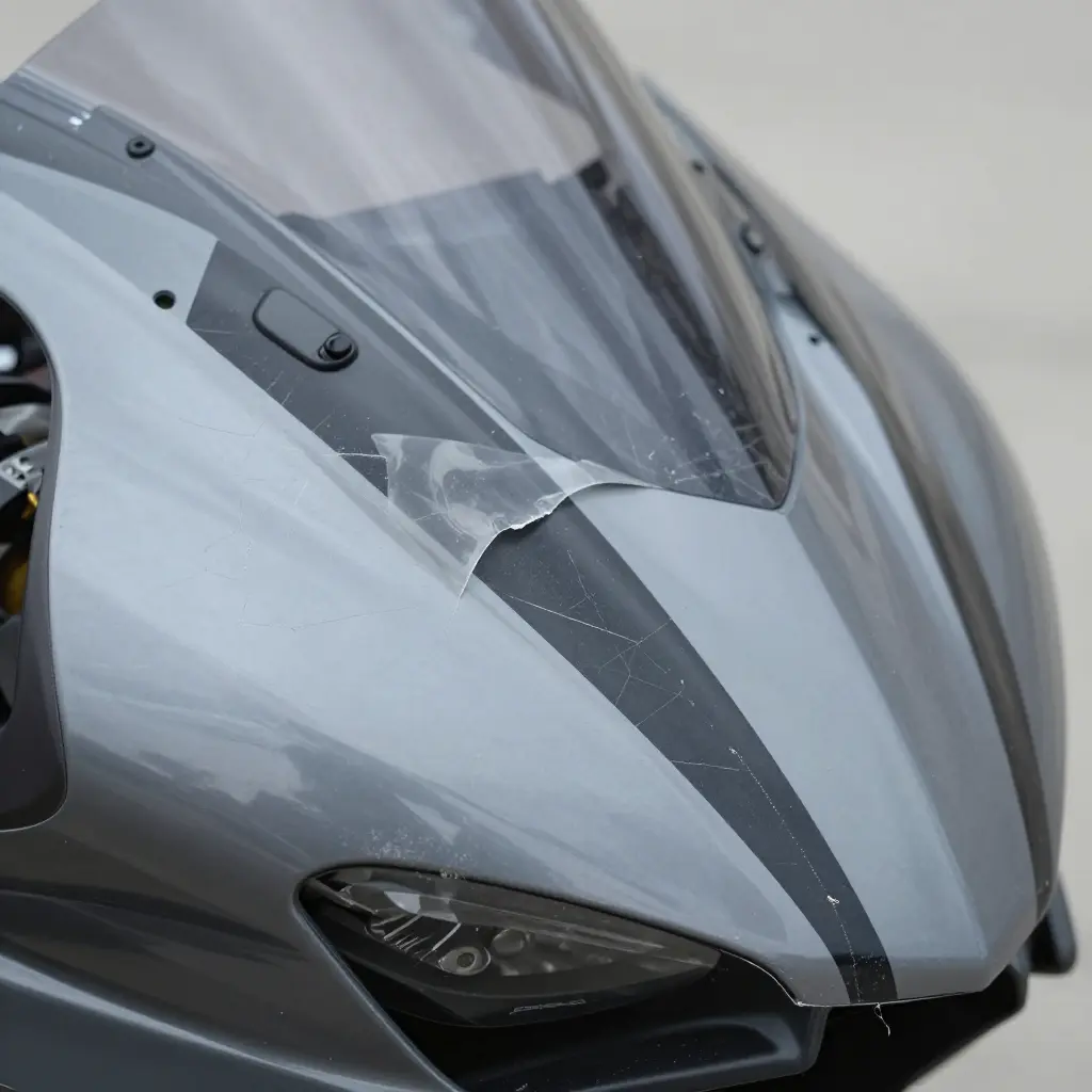 Close-up of a motorcycle fairing showing clear coat failure: a lifted decal edge, a hazy chalky patch, micro-cracking, and delamination along the decal border.